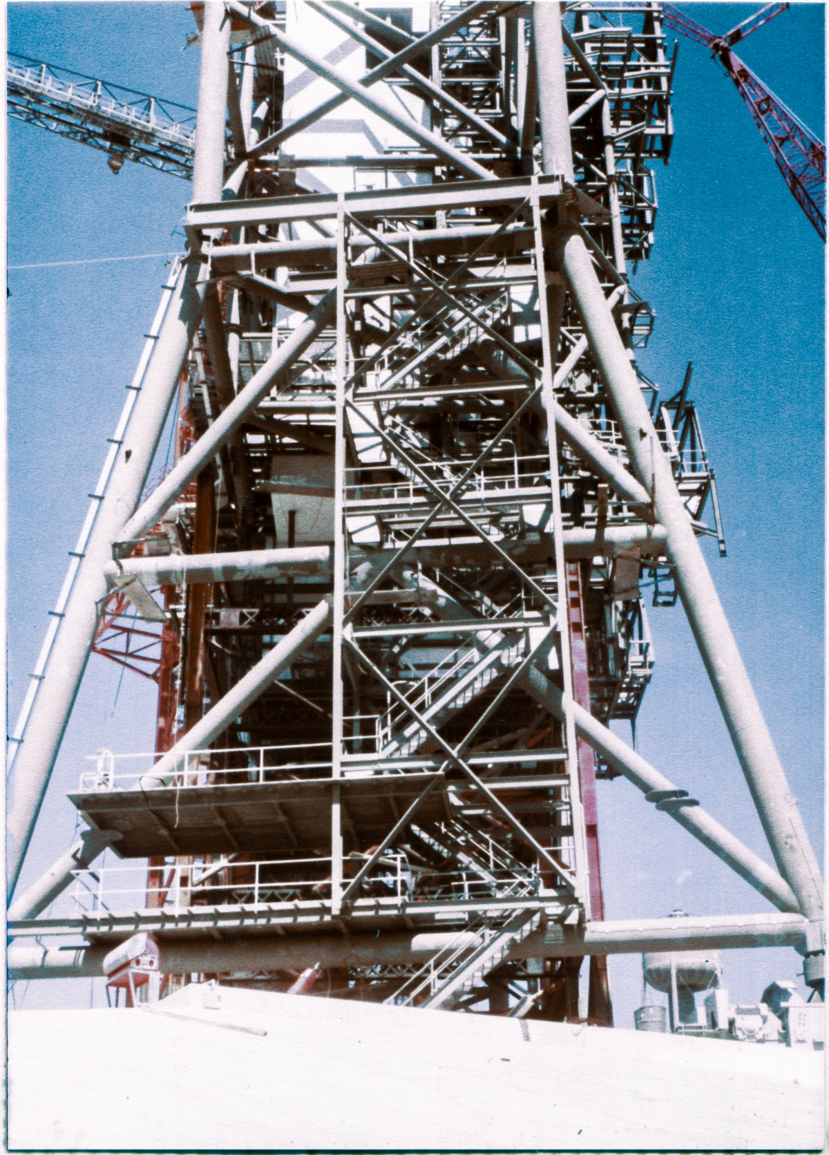 Image 017. From a vantage point roughly half-way down the west margin of the Pad Slope, south of the towers at Space Shuttle Launch Complex 39-B, Kennedy Space Center, Florida, you are looking back up at the Rotating Service Structure at its far end, Column Line 7. Construction was ongoing at this time, and the RSS was still partially-supported on falsework, but the main elements of the structure as it was originally designed are mostly in-place at this time. Photo by James MacLaren.